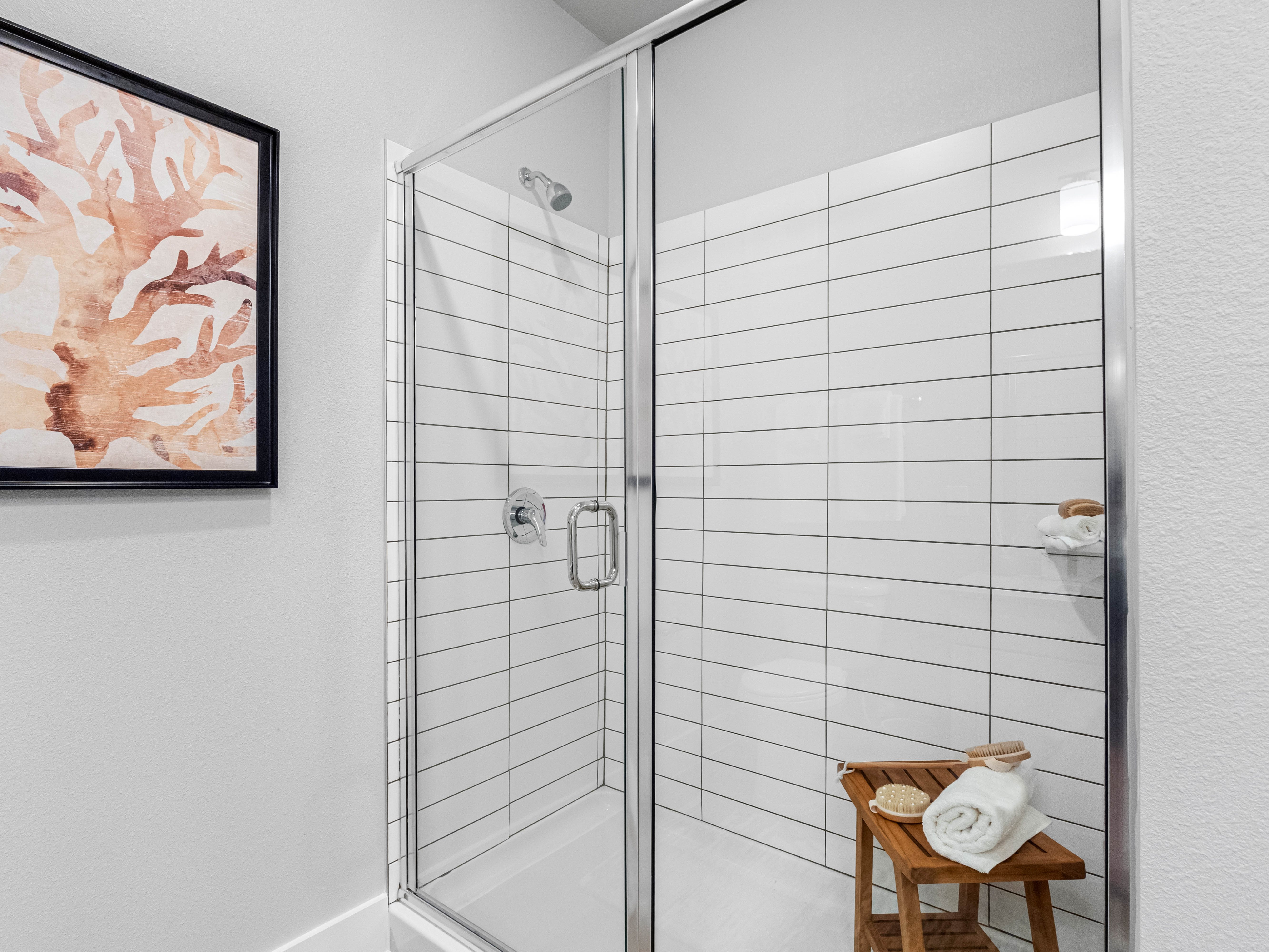 A bathroom with a glass shower door and a wooden stool with towels on it.